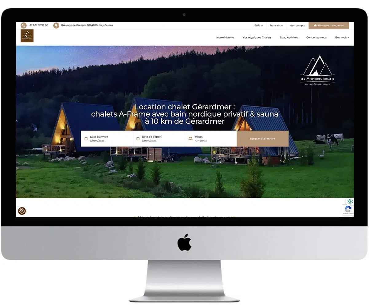 Mockup iMac présentant le site Les Atypiques Chalets avec chalets A-Frame en bois illuminés au crépuscule près de Gérardmer